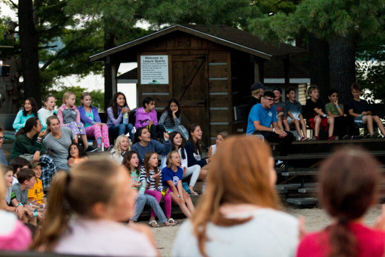 A group of children sit outside at camp with a counsellor.