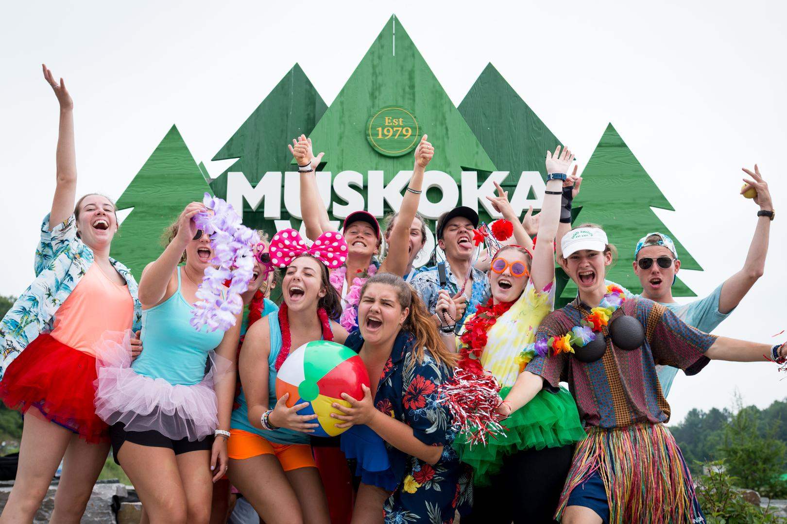 Teenagers dressed in bright colours in front of the Muskoka Woods sign